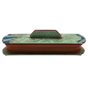 May include: A rectangular, Art Deco-style ceramic box with a lid. The box is primarily brown with a green lid and accents of blue and red. The lid has a handle and the box sits on a matching base.