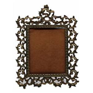 May include: Ornate, antique-style picture frame with a rectangular opening. The frame is made of a bronze-colored metal and features intricate, swirling floral and leaf designs. The interior has a brown backing, creating a contrast with the metallic frame.