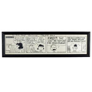 May include: Framed Peanuts comic strip in black and white. The strip features several panels with dialogue bubbles. The text includes phrases like "The teachers strike is over" and "Fired?!" The frame is black.