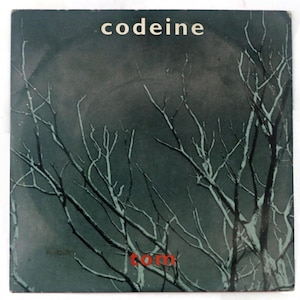 May include: Album cover with the word "codeine" in white at the top. The background is a dark gray with a large, blurred circle. White tree branches are in the foreground. The word "tom" is in red at the bottom.