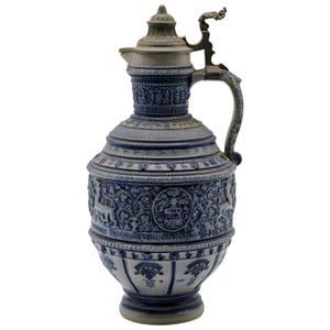 May include: A blue and gray ceramic pitcher with intricate relief designs, including figures, floral patterns, and a crest. It features a hinged metal lid and handle, showcasing a classic, ornate style.