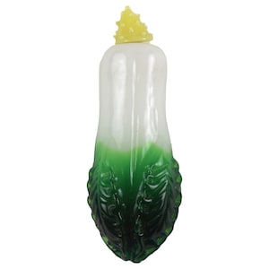 May include: A decorative bottle stopper shaped like a daikon radish. The stopper features a white body with a gradient of green at the base, and a yellow, textured top. The design mimics the appearance of a fresh vegetable.