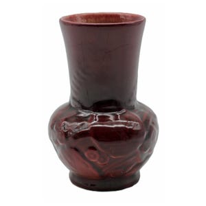 May include: A maroon-colored ceramic vase with a bulbous base and a flared top. The vase has a textured surface with a floral design. The vase is approximately 6 inches tall.