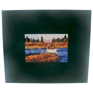 May include: A framed landscape print featuring a serene lake scene. The artwork depicts a boat with people on the water, surrounded by autumn foliage and trees. The frame is a dark green color.