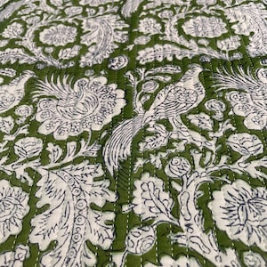 Puede incluir: Primer plano de un textil estampado en verde y blanco. El diseño presenta un patrón repetido de pájaros, flores y follaje estilizados. La tela está acolchada con costuras blancas, creando una superficie texturizada. La paleta de colores es principalmente verde y blanco.