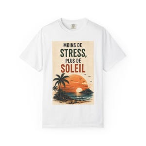 Peut inclure: Un t-shirt blanc à manches courtes avec une impression graphique rectangulaire représentant un coucher de soleil sur l'océan avec des palmiers et le texte MOINS DE STRESS, PLUS DE SOLEIL en lettres vert foncé et orange au-dessus du paysage.