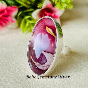 May include: A silver ring featuring an oval-shaped gemstone with a mix of burgundy, white, and yellow hues. The ring has a polished silver band and a bezel setting. The text "BohoGemstoneSilver" is visible at the bottom of the image. The ring is a piece of jewelry.
