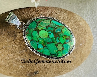 May include: Oval pendant with a vibrant green and turquoise stone set in a silver-colored metal frame. The stone has a mosaic-like pattern with brown and blue accents. The pendant has a bail for a chain and the text "BohoGemstoneSilver".