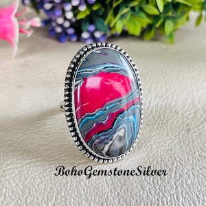 May include: Silver ring with an oval, multi-coloured stone. The stone has a striking pattern of pink, grey, blue, and white. The ring is set in a silver band with a beaded border. The text "BohoGemstoneSilver" is visible.