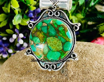 May include: A silver pendant necklace with a large, round, green and gold stone. The stone is set in a decorative silver frame with ornate details. The necklace has a silver chain and the text "BohoGemstoneSuper" is visible.