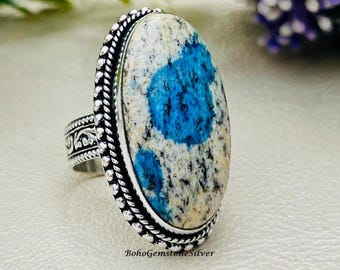 May include: A silver ring featuring an oval k2 stone with blue and white patterns. The ring has a decorative band and a beaded border around the stone. The text "BohoGemstoneSilver" is visible on the ring.