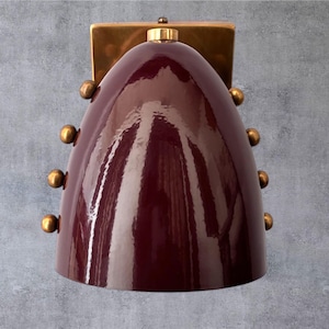 Può includere: Applique da parete bordeaux con finitura lucida. L'applique ha un paralume arrotondato a forma di campana con dettagli in ottone e una piastra di montaggio rettangolare in ottone. Design moderno della metà del secolo.