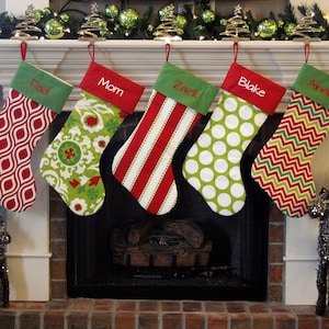 May include: Five personalized Christmas stockings hanging on a white mantel above a fireplace. The stockings are red, green, and white with different patterns and the names "Dad", "Mom", "Zack", "Blake", and "Ainsley" are embroidered on them.