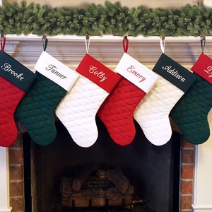 May include: Six personalized Christmas stockings hanging on a white mantel. The stockings are red, green, and white with quilted fabric and embroidered names: Brooke, Tanner, Colby, Emory, Addison, and Dylan.
