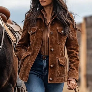 May include: A brown suede jacket with four front pockets and button fastenings. The jacket is worn over a brown collared shirt and paired with blue jeans. The overall style is Western-inspired.