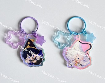 May include: Two anime-style keychains. One features a character in a black witch hat, the other in a white hat. Each keychain has a star and a star-shaped charm. The keychains are attached to a purple and blue ring.