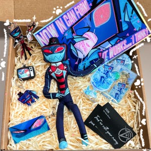 Könnte beinhalten: Eine Box voller Merchandise mit einer Cartoonfigur. Zu den Artikeln gehören eine Plüschpuppe, Schlüsselanhänger, Acryl-Charms und ein großer Druck mit dem Text "NOW IN CAN FORM" und "WORKS... I THINK?". Das Farbschema ist hauptsächlich blau, rot und schwarz.