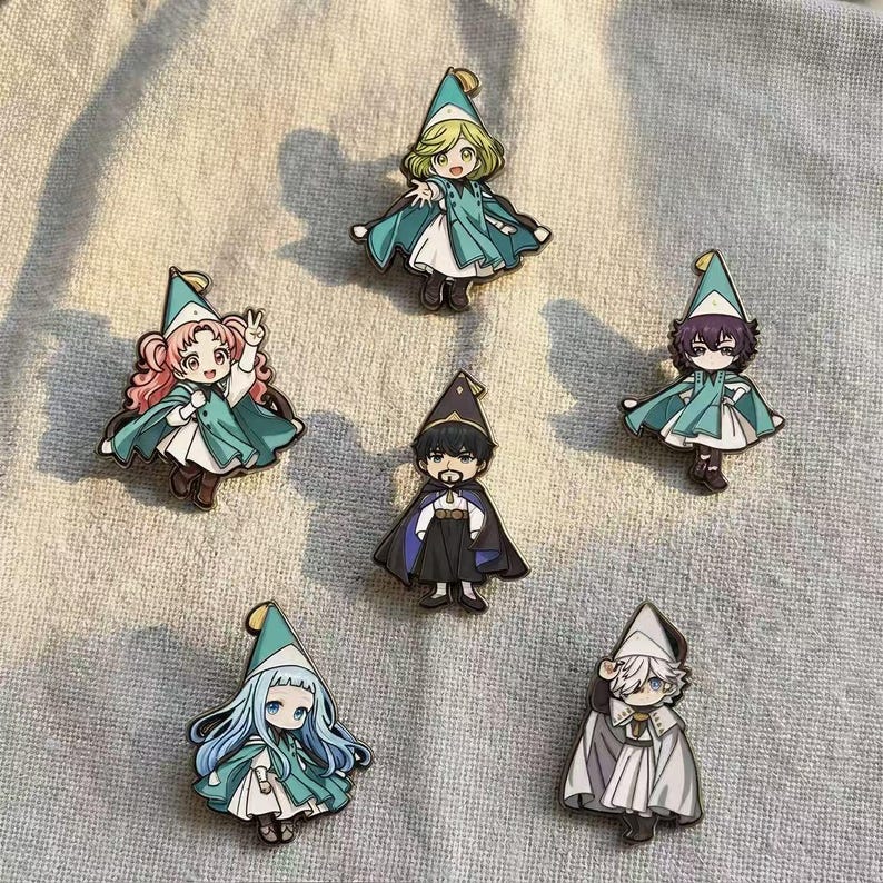 May include: Six enamel pins featuring chibi-style characters wearing pointed hats and capes. The characters have distinct hair colors including blonde, pink, dark purple, black, light blue, and white, each dressed in layered outfits with capes.