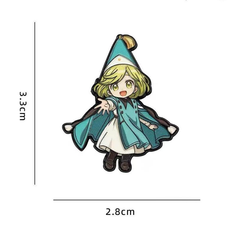 May include: A cartoon-style enamel pin featuring a blonde character wearing a teal pointed hat and matching cape over a white dress. The character has one hand extended forward. The pin measures 3.3 cm in height and 2.8 cm in width.