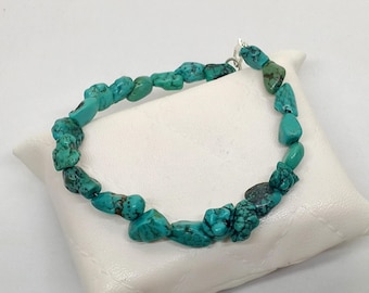 Può includere: Un braccialetto con schegge di turchese con chiusura argentata. Il braccialetto è composto da pietre di turchese irregolari e lucide in varie tonalità di blu-verde. Le pietre sono infilate insieme per formare un cerchio completo.
