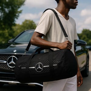 Könnte beinhalten: Schwarze Reisetasche mit silbernem Mercedes-Benz-Logo und Akzenten. Die Tasche hat einen Schultergurt. Im Hintergrund ist ein schwarzer Mercedes-Benz SUV zu sehen.