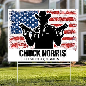 May include: A white yard sign featuring a silhouette of a man in a cowboy hat holding two guns, set against a distressed American flag. The sign reads "CHUCK NORRIS DOESN'T SLEEP, HE WAITS."