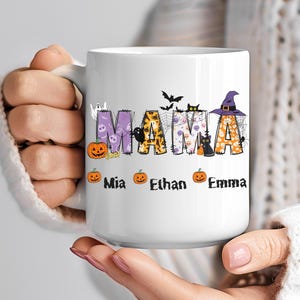 Könnte beinhalten: Weiße Keramik-Tasse mit dem Wort "MAMA" in farbenfrohen Halloween-Buchstaben. Die Buchstaben sind mit Kürbissen, Fledermäusen, Katzen und einem Hexenhut verziert. Die Namen "Mia", "Ethan" und "Emma" sind darunter gedruckt.