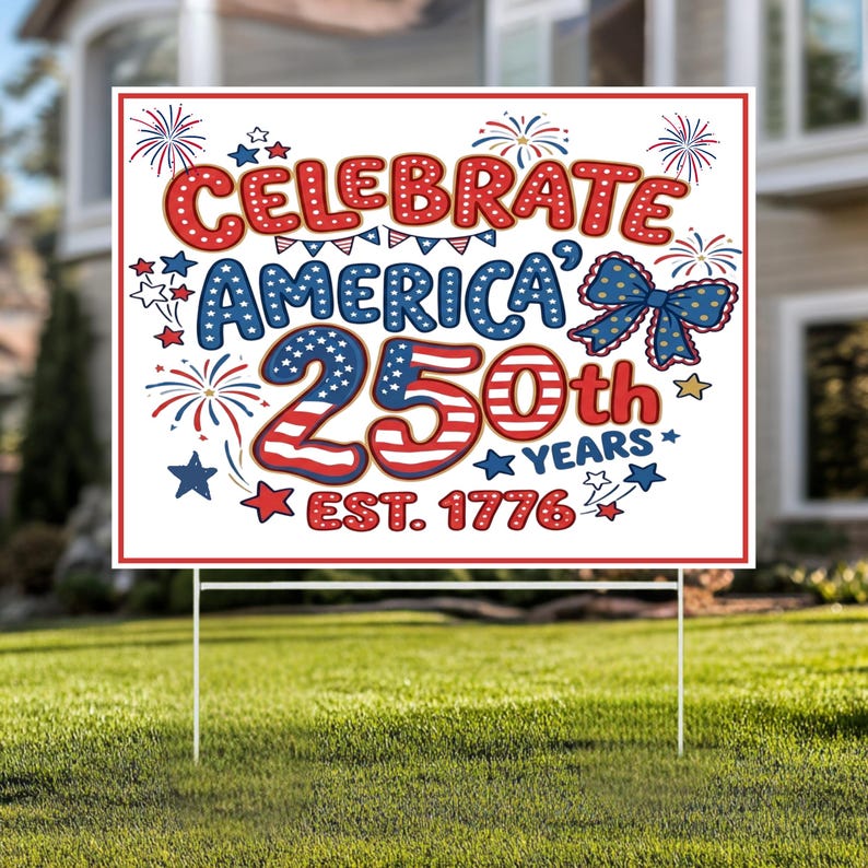 May include: A white yard sign with red and blue text that reads "Celebrate America 250th Years Est. 1776." The sign has a red border and is decorated with stars, fireworks, and a blue bow.