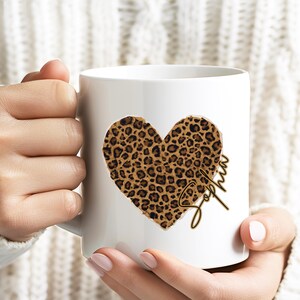 Könnte beinhalten: Weiße Keramik-Tasse mit einem herzförmigen Leopardenmuster. Auf der Tasse steht der Name "Sophia" in Schreibschrift. Die Tasse wird von einer Person gehalten.