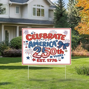 May include: A white sign with red, white, and blue text that reads "Celebrate America 250th Years Est. 1776." The sign has a red border and is decorated with fireworks, stars, and a bow. It is displayed on a green lawn.