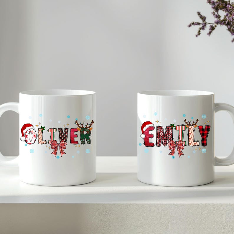 K&ouml;nnte beinhalten: Zwei wei&szlig;e Keramikbecher mit den Namen "Oliver" und "Emily" in festlicher Schrift. Die Namen sind mit Weihnachtselementen wie Weihnachtsm&uuml;tzen, Rentiergeweihen und Schleifen verziert. Die Becher stehen auf einer wei&szlig;en Oberfl&auml;che.