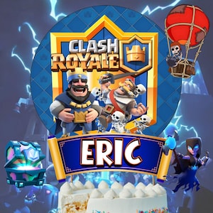 May include: A Clash Royale themed cake topper with the name "ERIC" on a blue banner. The topper features characters from the game, including a king, skeletons, and a red hot air balloon. The cake is white with frosting and sprinkles.