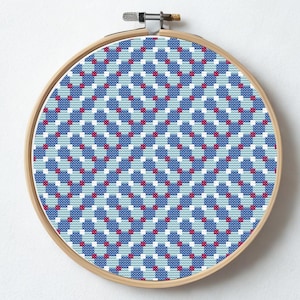 Puede incluir: Un bastidor de bordado redondo con un patrón geométrico en tonos azules, blancos y rojos. La palabra "Tessellate" se muestra encima del diseño, y "Piesling stitch face" está escrito debajo. El bastidor de madera sostiene la obra bordada.