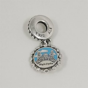 Può includere: Un charm in argento con un ciondolo rotondo raffigurante Santa Sofia a Istanbul, Turchia, su uno sfondo di cielo blu. Il charm è circondato da un bordo a forma di cuore e presenta la scritta "Hagia Sophia".