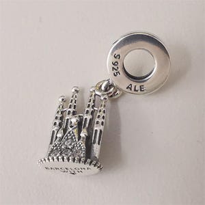Puede incluir: Un charm de plata con la basílica de la Sagrada Familia en Barcelona. El charm tiene intrincados detalles arquitectónicos y acentos brillantes. El charm está unido a un anillo de plata con las marcas "S925" y "ALE". La base del charm dice "BARCELONA WITH".