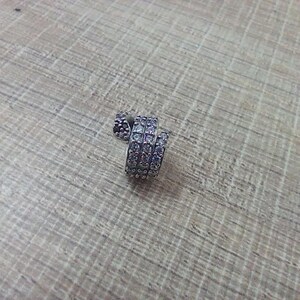 May include: A silver-toned charm bead featuring a spiral design encrusted with numerous small, clear, sparkling stones. The cylindrical piece has a metallic finish and a textured surface created by the dense arrangement of the embedded stones.