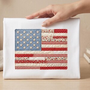 Puede incluir: Un lienzo blanco con un diseño de bandera estadounidense de tela. El campo azul de la bandera tiene 50 estrellas de madera. Las rayas están hechas de telas rojas y blancas estampadas. El lienzo está sostenido por una mano.