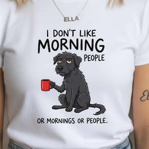 May include: White t-shirt featuring a cartoon dog holding a red mug. The dog has a sleepy expression and the shirt reads "I don't like morning people or mornings or people."