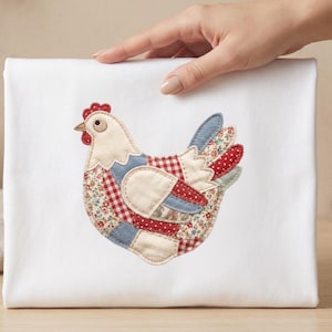 May include: A white fabric item featuring a patchwork chicken design. The chicken has a cream-colored body, red comb, and a patchwork of red, blue, and floral fabrics. The item is held by a hand.