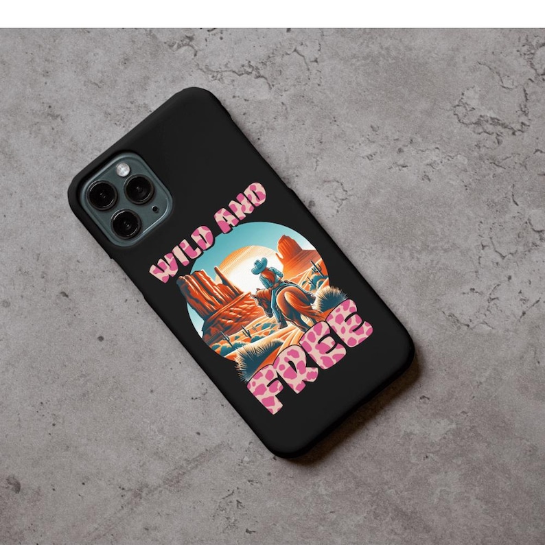 May include: Black phone case featuring a desert landscape with a cowboy on horseback. The words "WILD AND FREE" are printed in a pink, patterned font. The case has a glossy finish and a camera cutout.