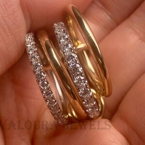 Puede incluir: Un anillo de oro con múltiples bandas, algunas incrustadas con pequeñas piedras brillantes. El anillo se sostiene en una mano, mostrando su diseño. El anillo es una joya.