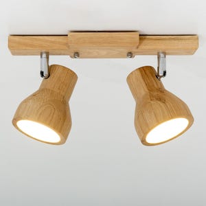 Peut inclure: Un plafonnier en bois avec deux spots orientables. Le luminaire est en bois clair et possède une base rectangulaire. Les spots sont orientés vers le bas et émettent une lumière chaude et vive.