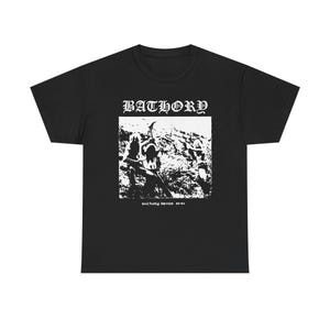 Könnte beinhalten: Schwarzes T-Shirt mit weißem Aufdruck. Der Aufdruck zeigt den Bandnamen "BATHORY" über einem Schwarz-Weiß-Bild von Figuren in einer Landschaft. Der Text "BATHORY DEMOS 83-84" steht darunter.