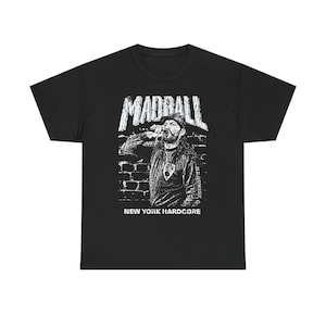 Puede incluir: Camiseta negra con un gráfico blanco desgastado que representa a una persona bebiendo de una botella, con el nombre de la banda "MADBALL" arriba y "NEW YORK HARDCORE" abajo. La imagen tiene un fondo de pared de ladrillos.