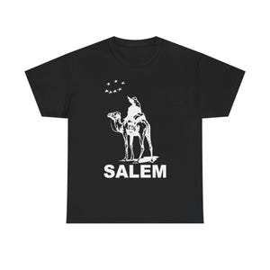 Könnte beinhalten: Schwarzes T-Shirt mit weißer Grafik einer Person auf einem Kamel unter Sternen. Das Wort "SALEM" ist darunter in Weiß gedruckt. Ein lässiges Unisex-T-Shirt.