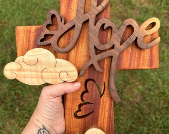 May include: Wooden cross with the word "Hope" carved in a decorative font. The cross is decorated with butterflies and clouds, all carved from wood.