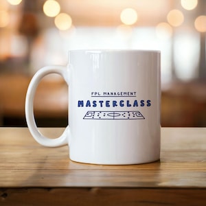 Könnte beinhalten: Weiße Keramiktasse mit dem blauen Schriftzug "FPL MANAGEMENT MASTERCLASS". Darunter befindet sich eine blaue Grafik eines Fußballfeldes. Die Tasse hat einen gebogenen Henkel und steht auf einer Holzoberfläche.