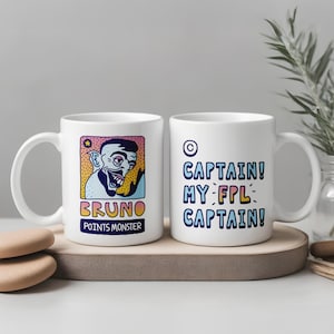 Könnte beinhalten: Zwei weiße Keramikbecher mit humorvollen Designs. Ein Becher zeigt ein Cartoon-Monster mit dem Namen "BRUNO" und dem Text "POINTS MONSTER". Der andere Becher hat den Text "CAPTAIN! MY-FPL-CAPTAIN!" in Blau, Gelb und Weiß.