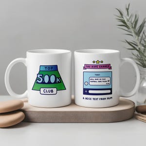Könnte beinhalten: Zwei weiße Keramikbecher mit humorvollem Text und Grafiken. Auf einem Becher steht "TOP 500K CLUB" in Grün und Blau. Der andere Becher hat eine Textblase mit der Aufschrift "YOU HAVE EARNED" und "A NICE TEXT FROM MUM".