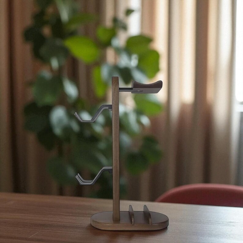 May include: A wooden headphone stand with a light brown finish. The stand has a vertical post with three curved metal hooks for hanging headphones and a top rest. The base is oval-shaped with slots for additional storage.